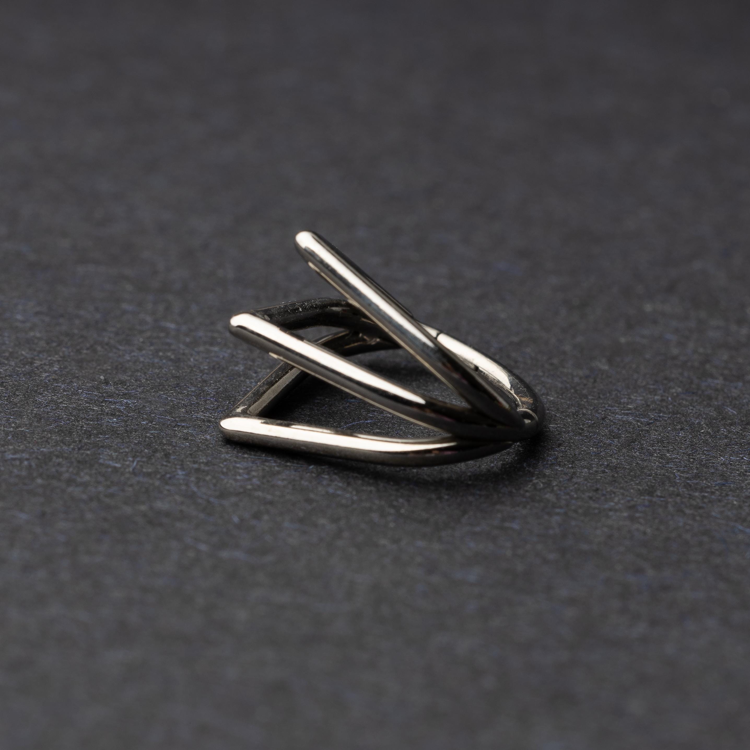 Close-up of a geometric septum clicker in silver, featuring a unique layered triangular design, displayed on a dark background.
