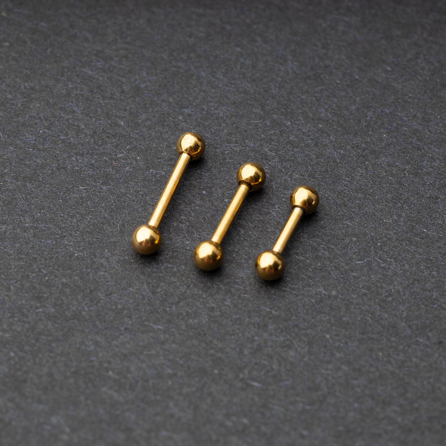 Gold-tone stainless steel barbells with polished spheres on a dark background.