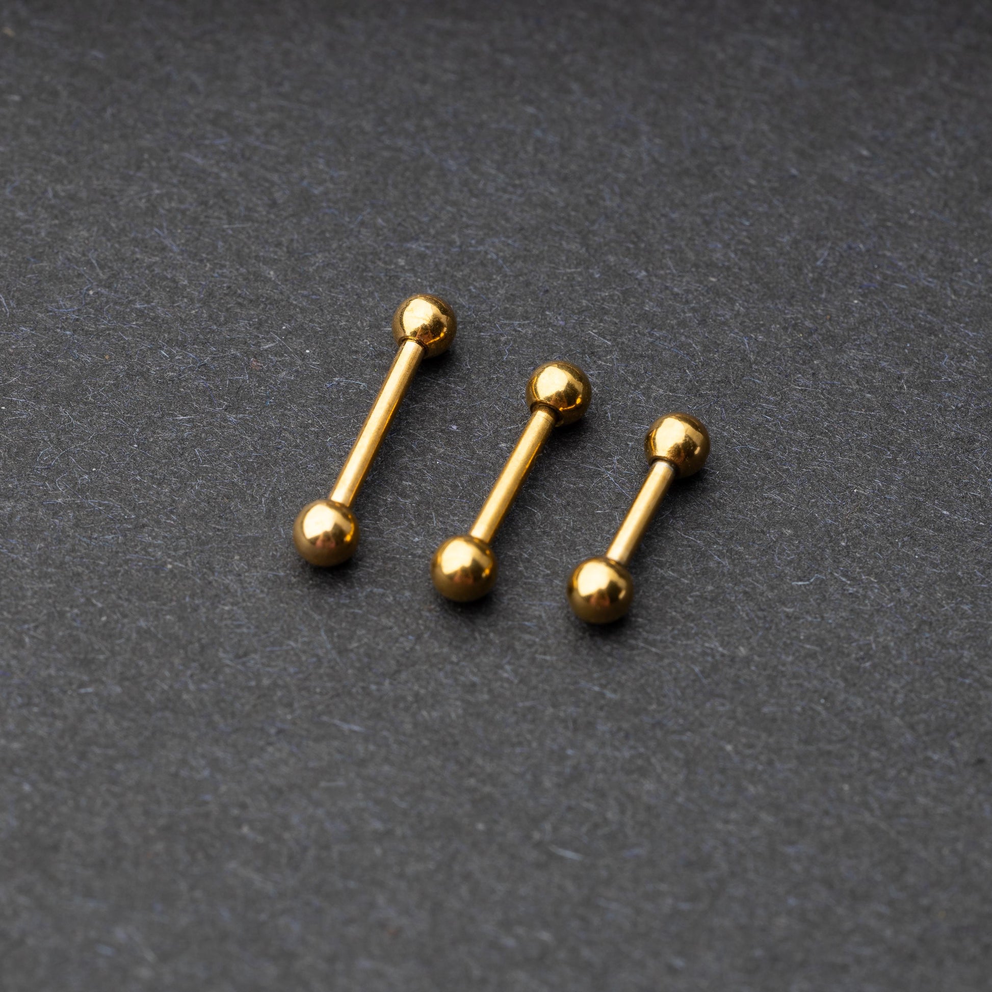 Gold-tone stainless steel barbells with polished spheres on a dark background.