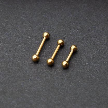 Gold-tone stainless steel barbells with polished spheres on a dark background.