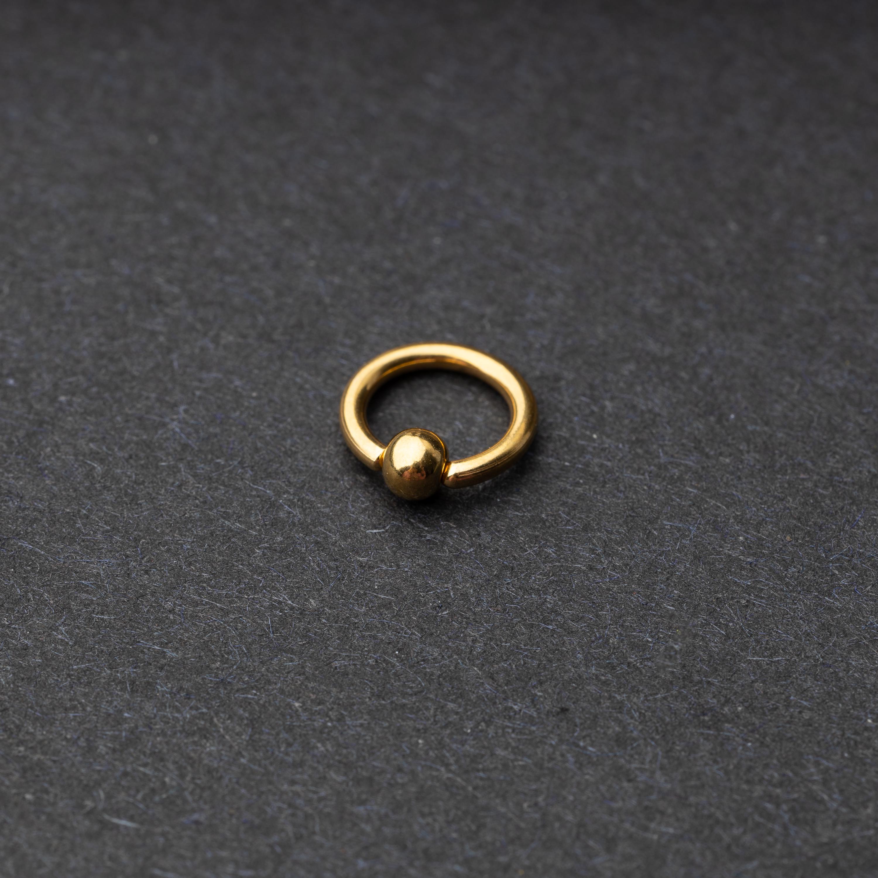 A gold-tone stainless steel captive bead rings displayed on a dark background.