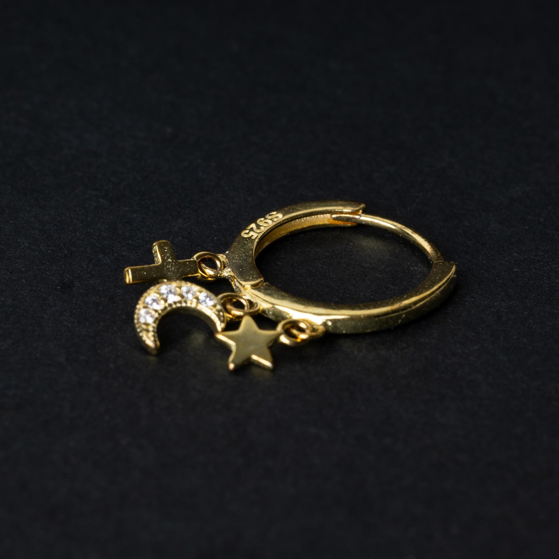 Gold clicker ring adorned with a moon charm encrusted with crystals, a star, and a cross, displayed on a dark background.