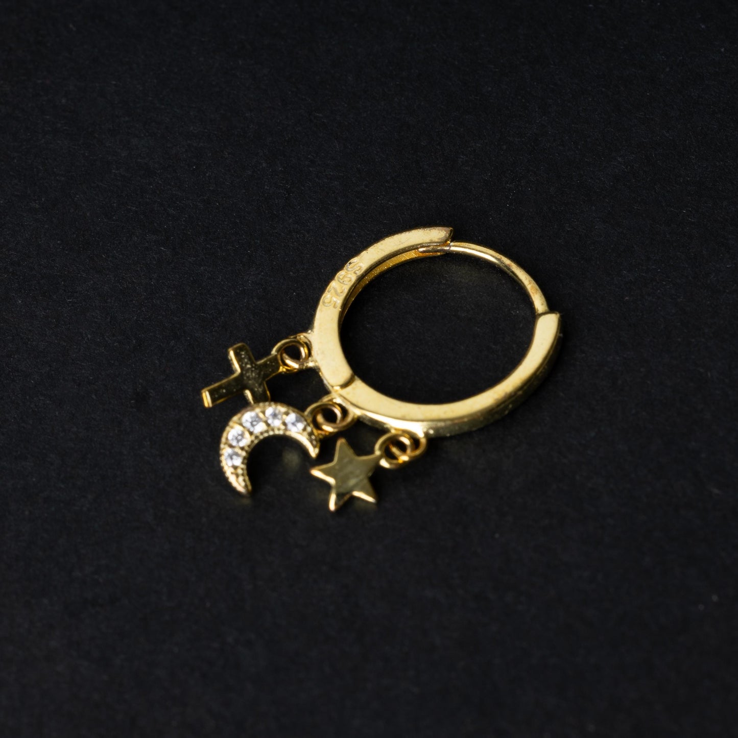Gold clicker ring adorned with a moon charm encrusted with crystals, a star, and a cross, displayed on a dark background.