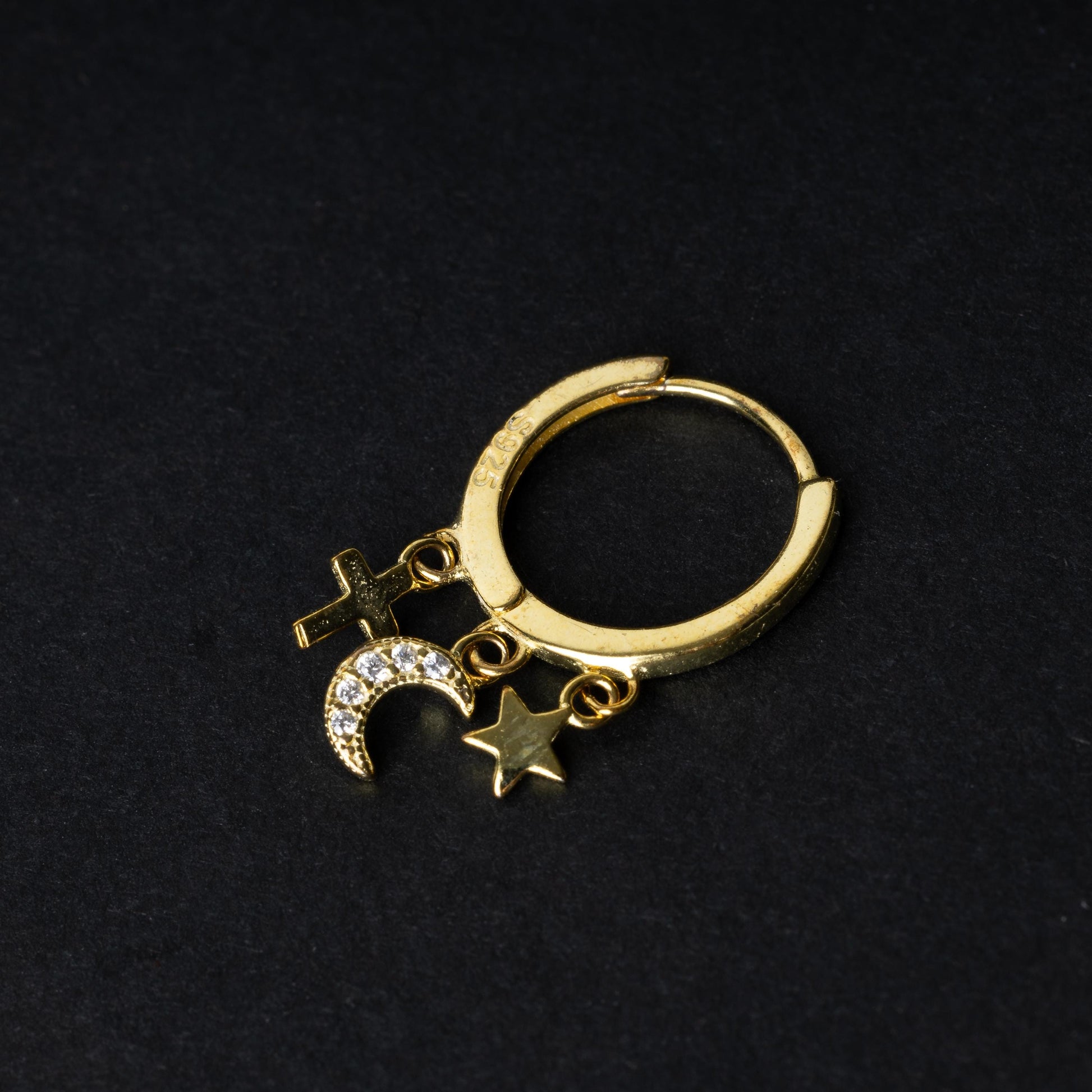 Gold clicker ring adorned with a moon charm encrusted with crystals, a star, and a cross, displayed on a dark background.