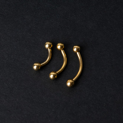 Gold curved barbells in three sizes with smooth ball ends, displayed on a dark background.