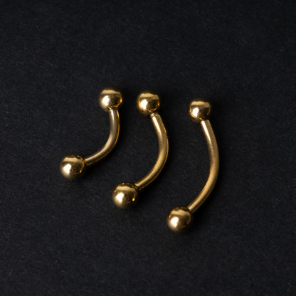 Gold curved barbells in three sizes with smooth ball ends, displayed on a dark background.