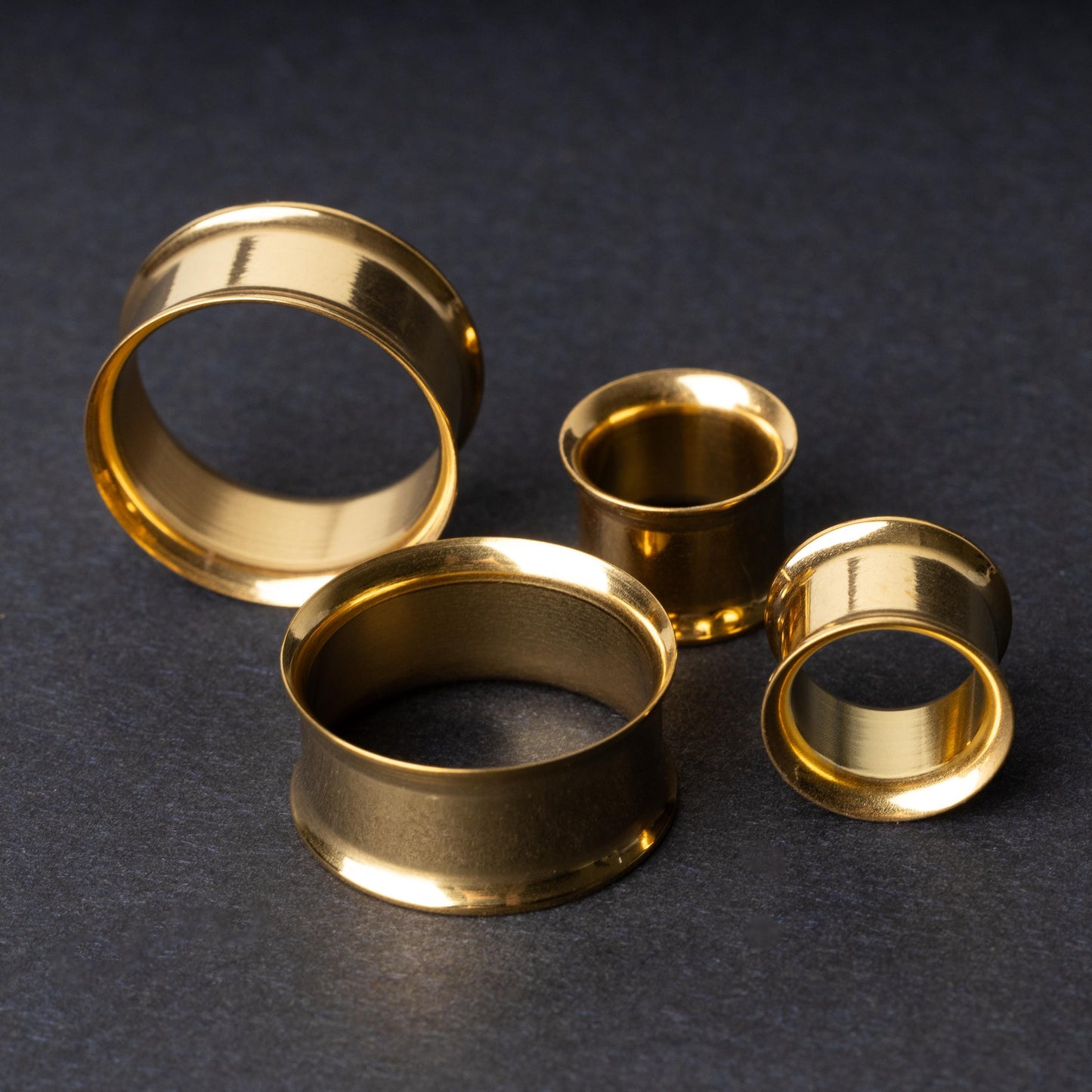 Gold double-flared tunnels in varying sizes, with a polished finish, displayed on a dark background.