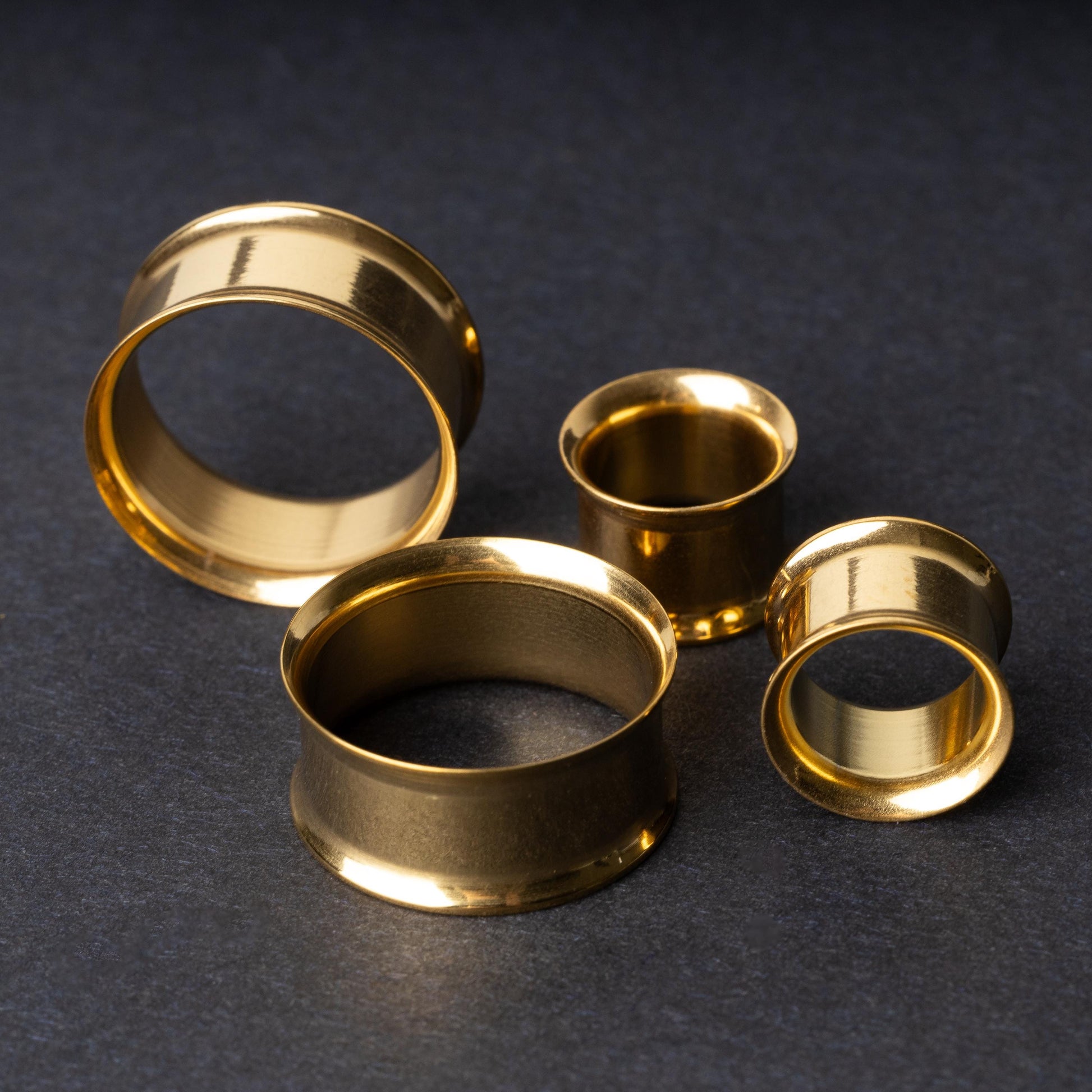 Gold double-flared tunnels in varying sizes, with a polished finish, displayed on a dark background.