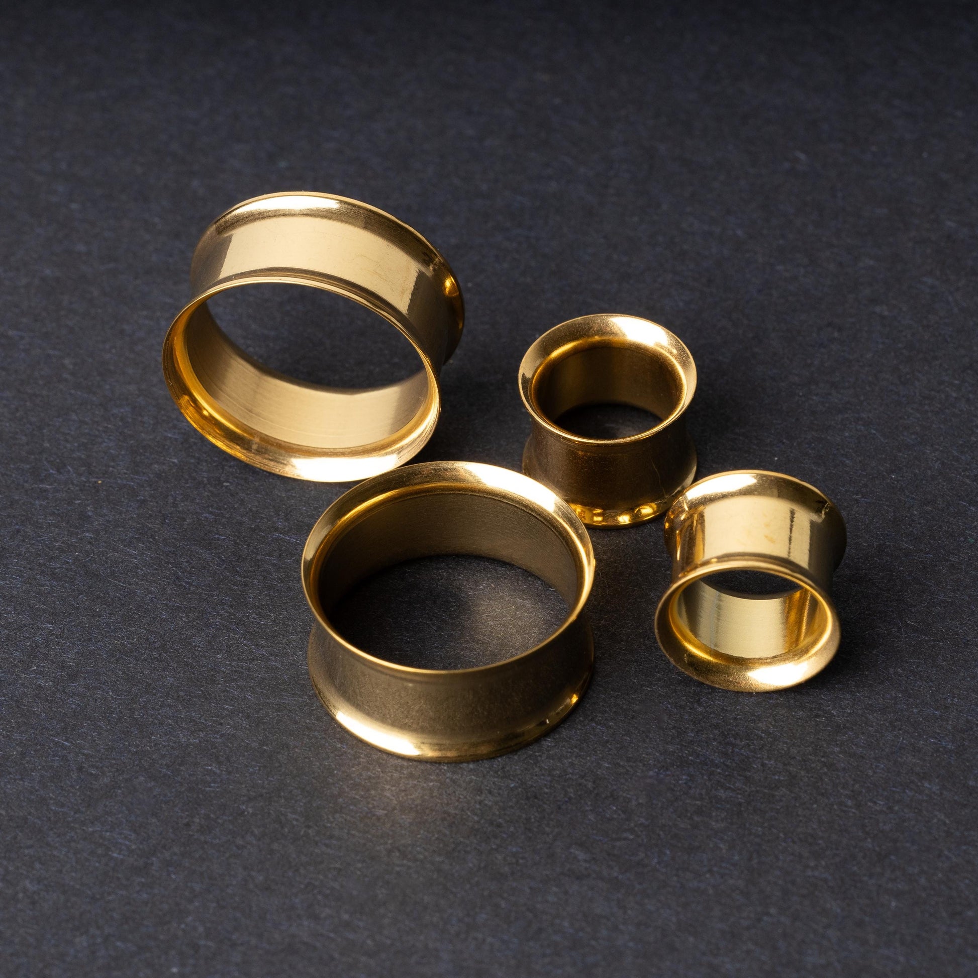 Gold double-flared tunnels in varying sizes, with a polished finish, displayed on a dark background.