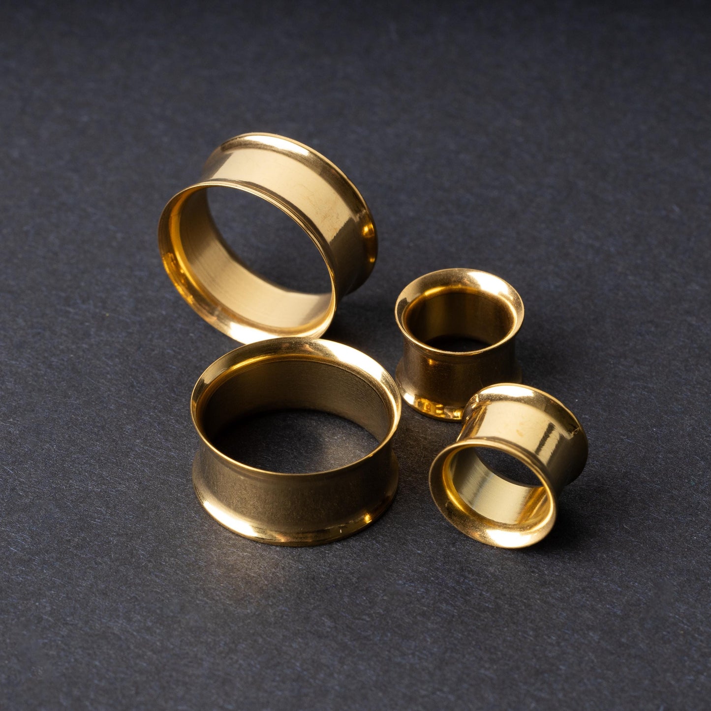 Gold double-flared tunnels in varying sizes, with a polished finish, displayed on a dark background.