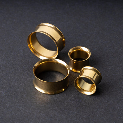 Gold double-flared tunnels in varying sizes, with a polished finish, displayed on a dark background.