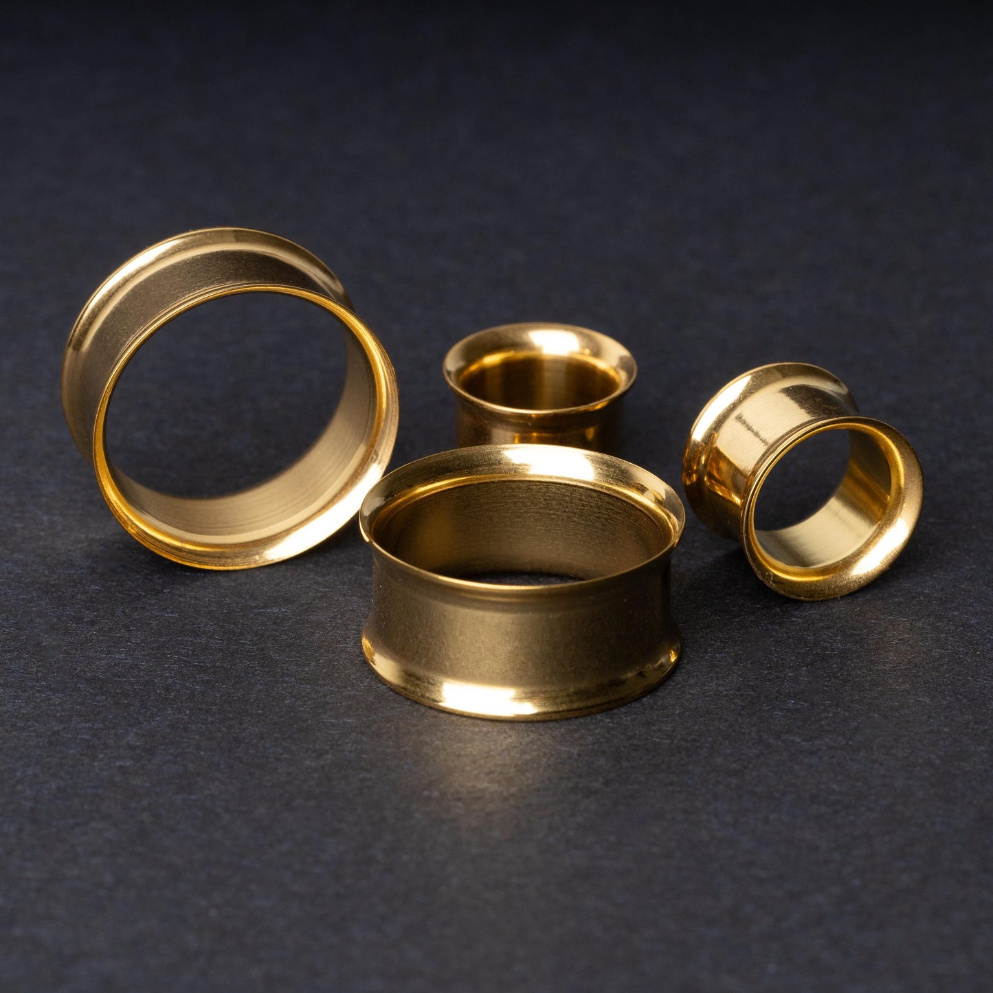 Gold double-flared tunnels in varying sizes, with a polished finish, displayed on a dark background.