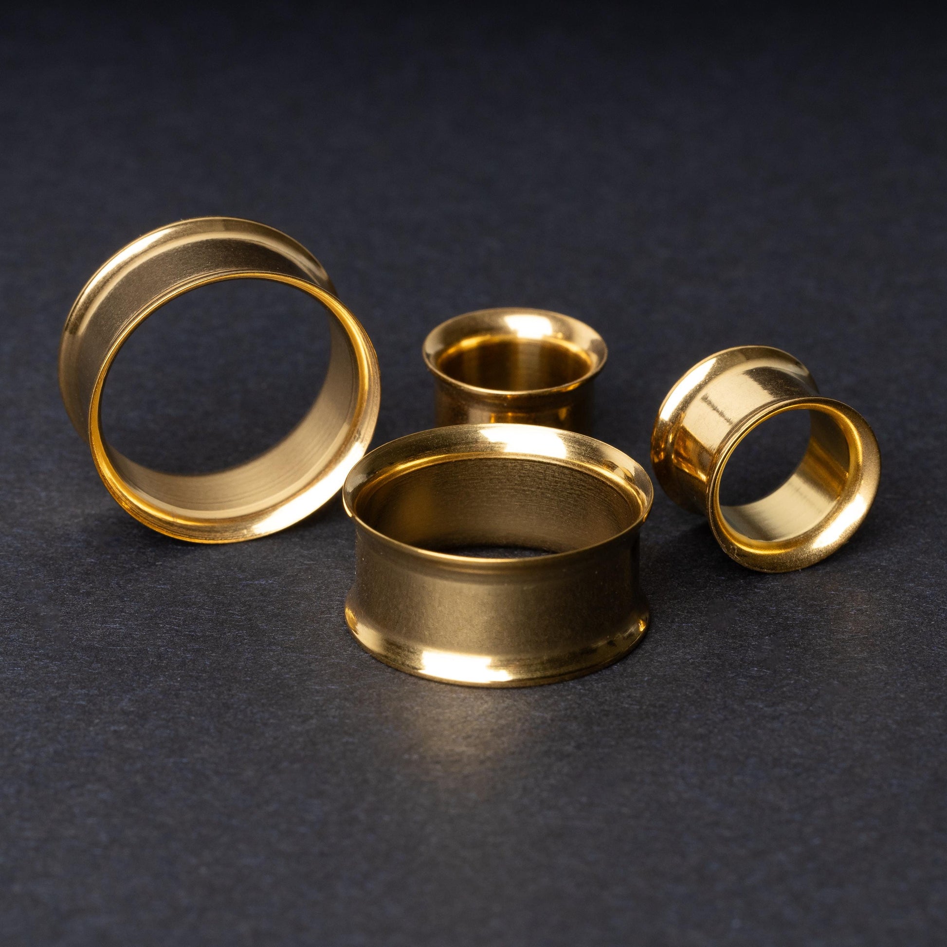 Gold double-flared tunnels in varying sizes, with a polished finish, displayed on a dark background.