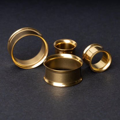 Gold double-flared tunnels in varying sizes, with a polished finish, displayed on a dark background.