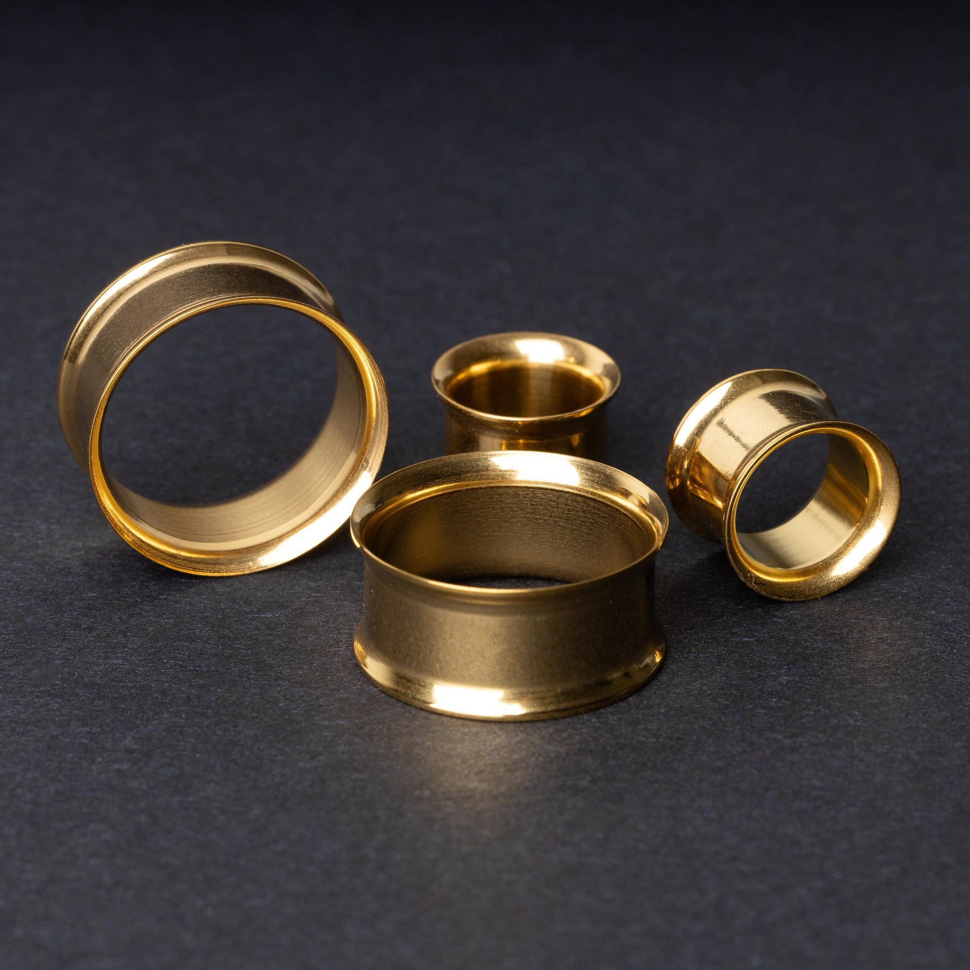 Gold double-flared tunnels in varying sizes, with a polished finish, displayed on a dark background.
