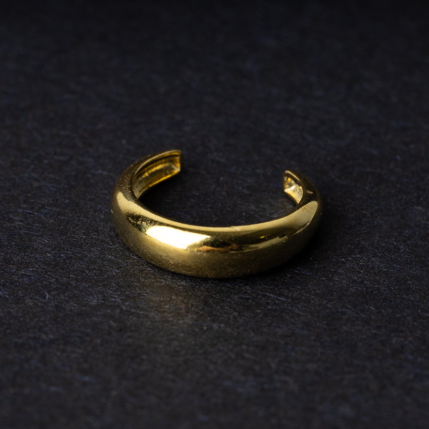 Bold ear cuff in gold with a smooth, domed design, displayed on a dark background.