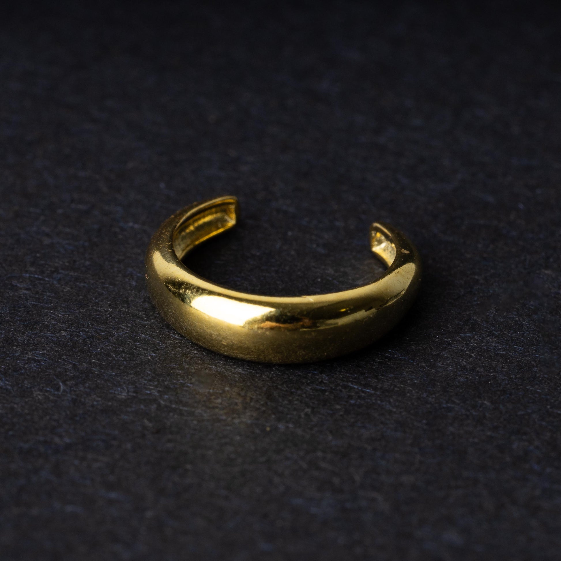 Bold ear cuff in gold with a smooth, domed design, displayed on a dark background.