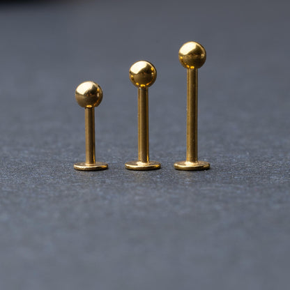 Gold labret studs with ball ends in three different lengths, displayed on a dark background.