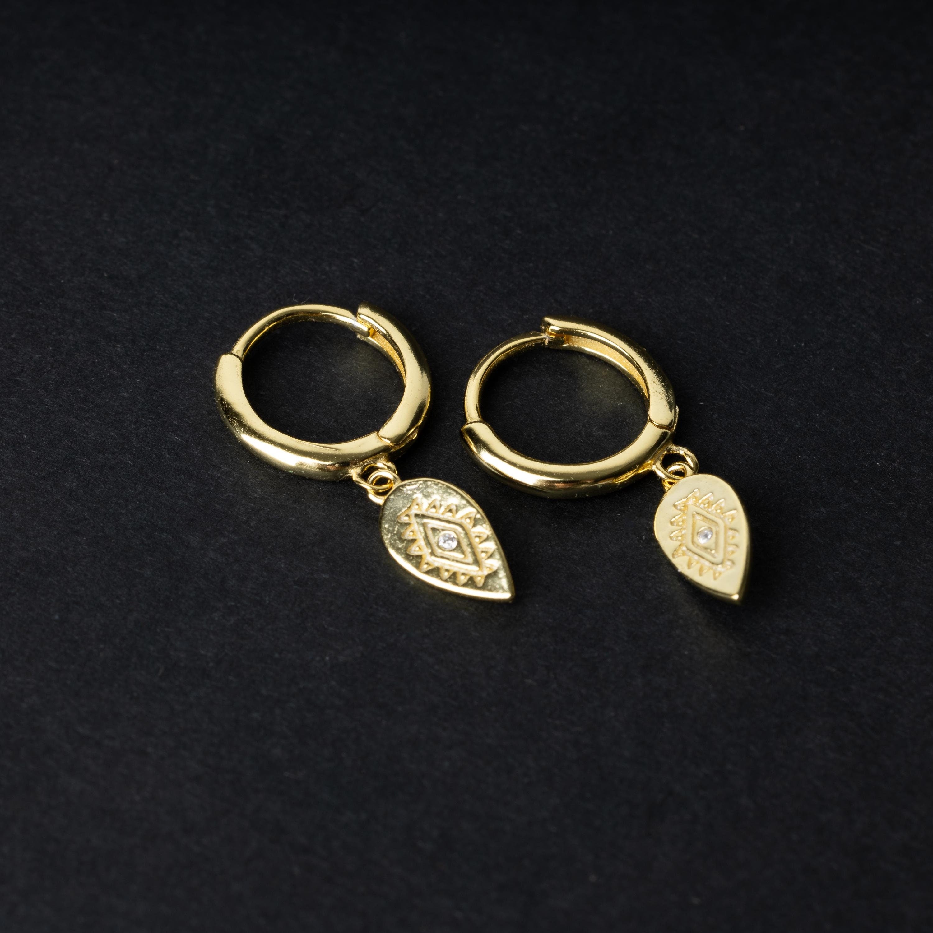 Gold hoop earrings with detailed teardrop-shaped charms, displayed on a dark background.