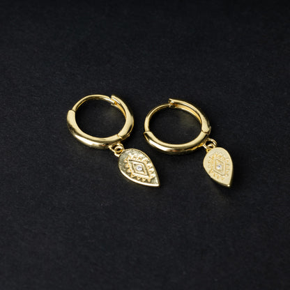 Gold hoop earrings with detailed teardrop-shaped charms, displayed on a dark background.