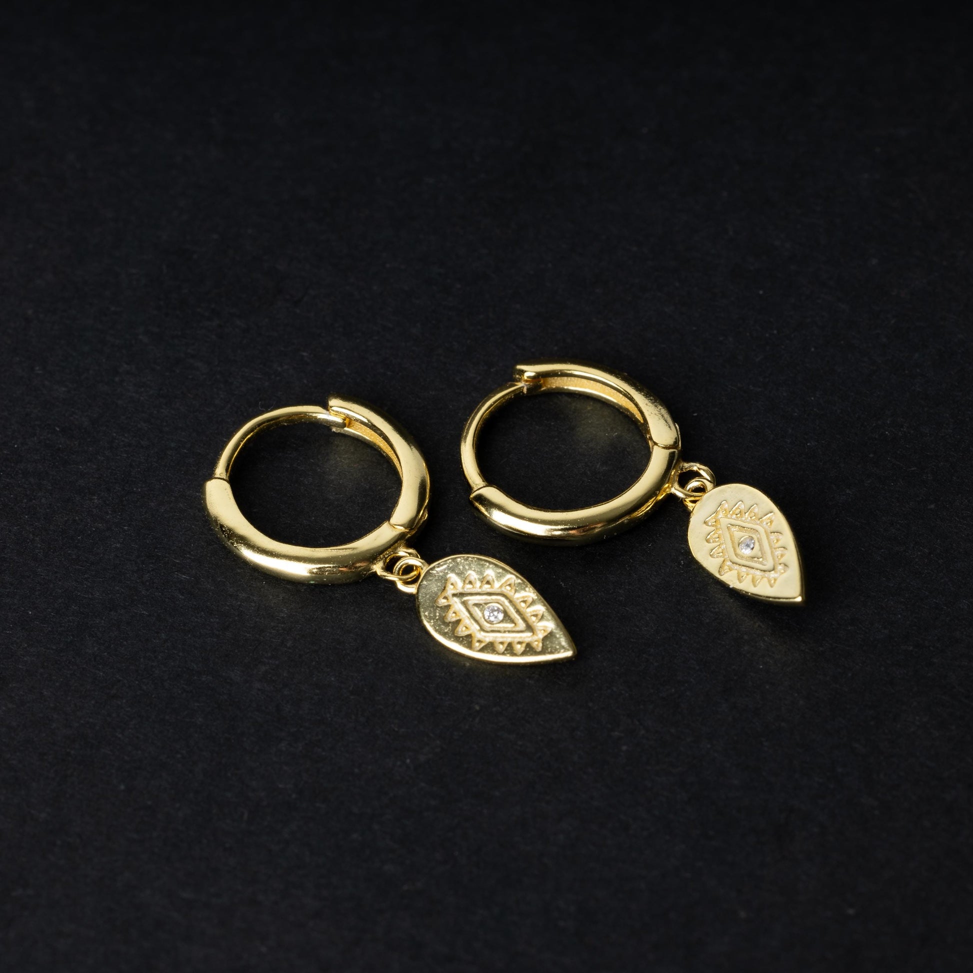 Gold hoop earrings with detailed teardrop-shaped charms, displayed on a dark background.