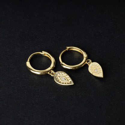 Gold hoop earrings with detailed teardrop-shaped charms, displayed on a dark background.