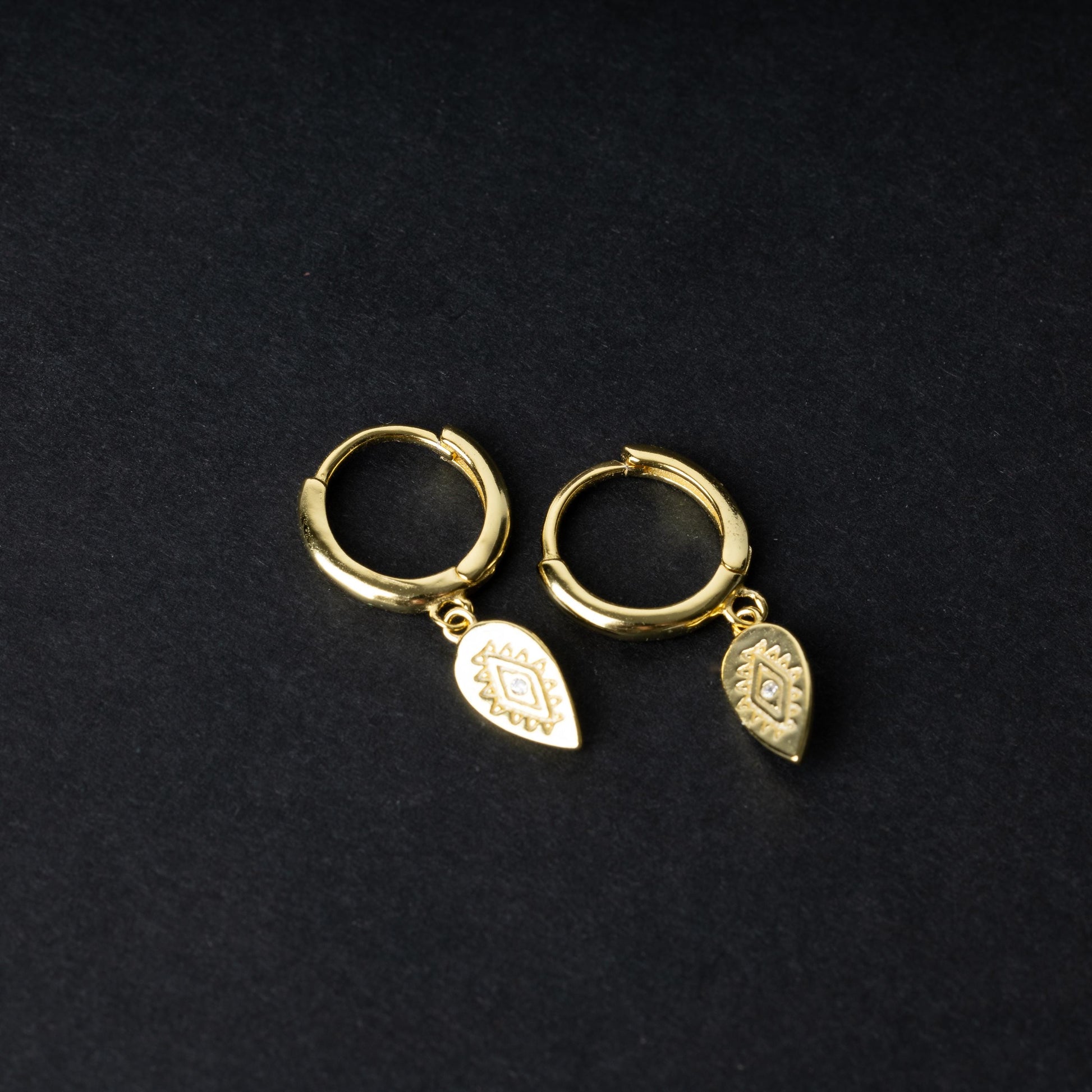 Gold hoop earrings with detailed teardrop-shaped charms, displayed on a dark background.