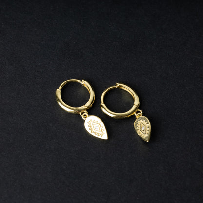 Gold hoop earrings with detailed teardrop-shaped charms, displayed on a dark background.
