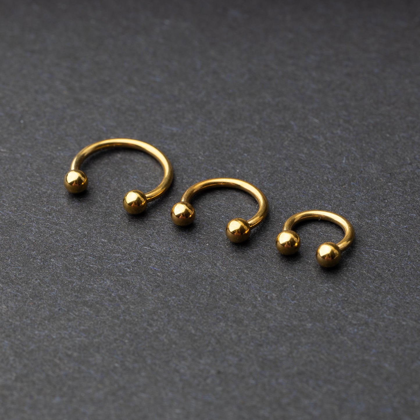 Gold horseshoe rings in three different sizes with ball ends, displayed on a dark background.