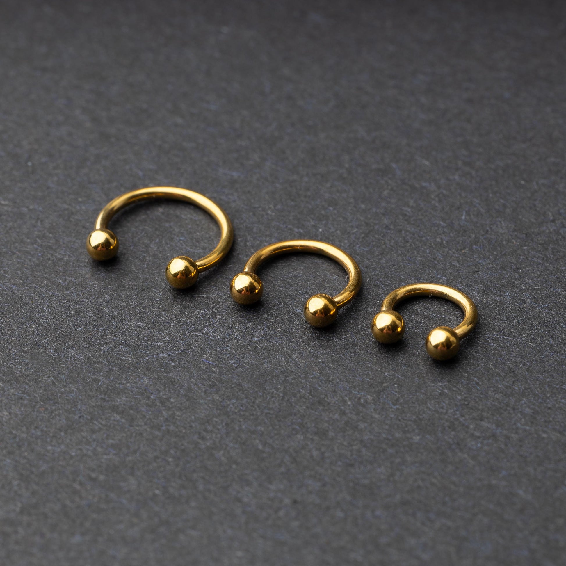 Gold horseshoe rings in three different sizes with ball ends, displayed on a dark background.