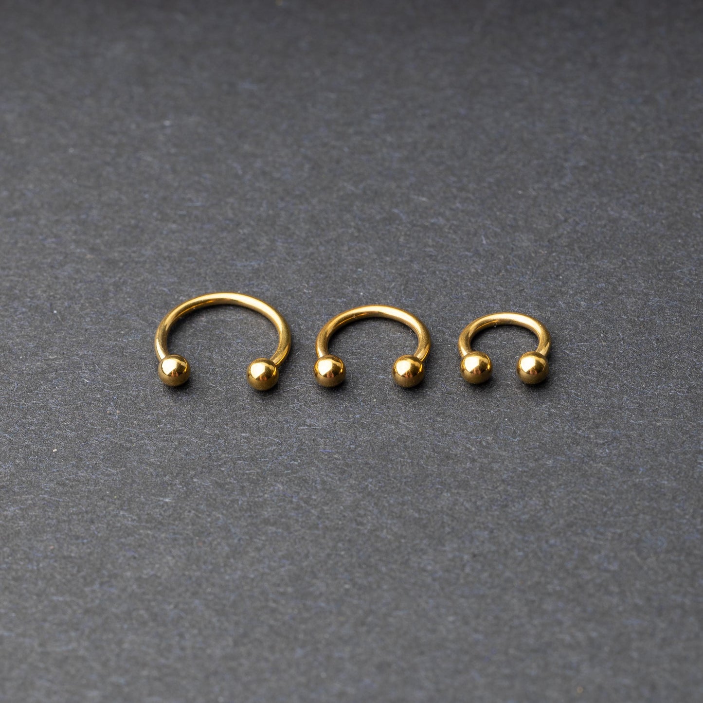 Gold horseshoe rings in three different sizes with ball ends, displayed on a dark background.