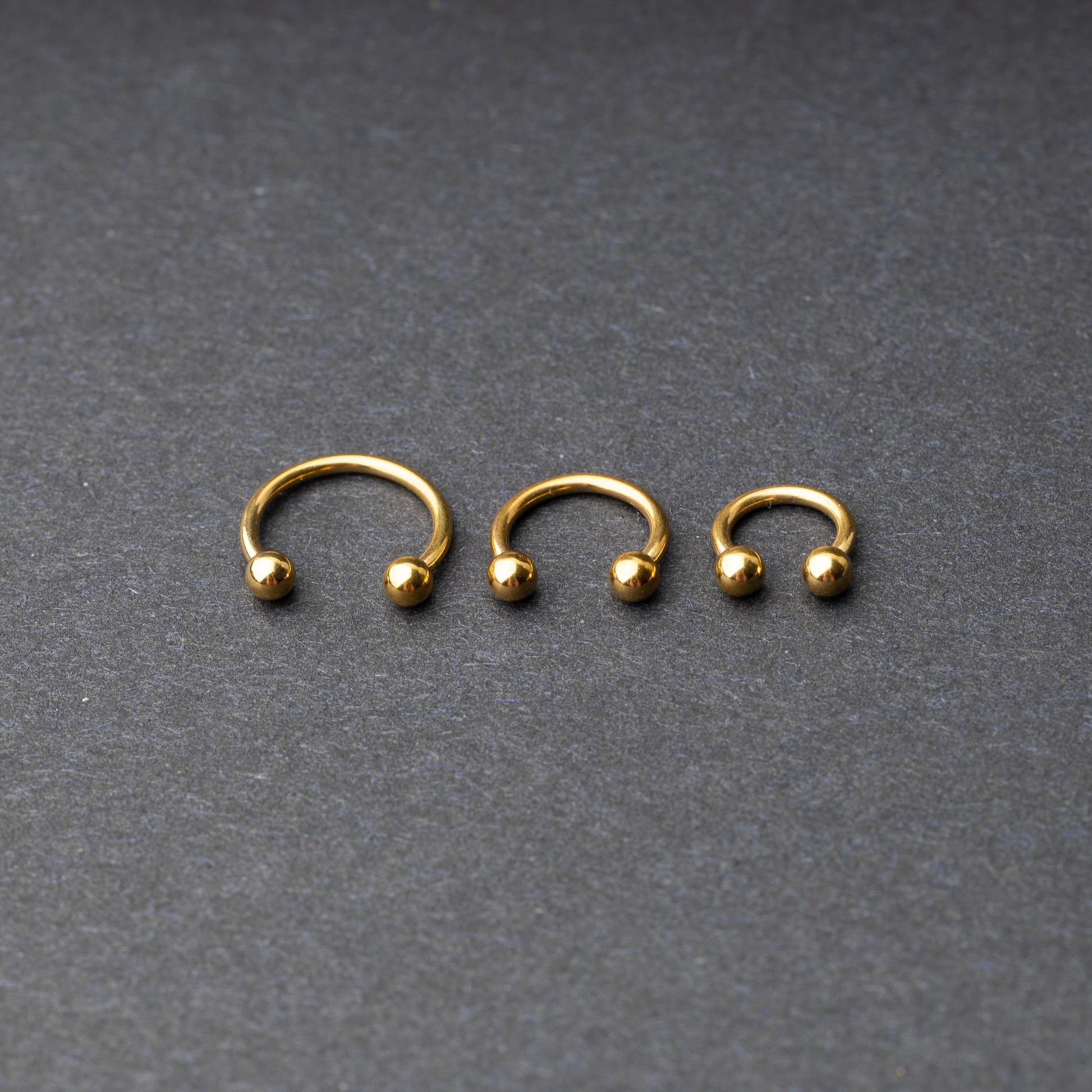 Gold horseshoe rings in three different sizes with ball ends, displayed on a dark background.