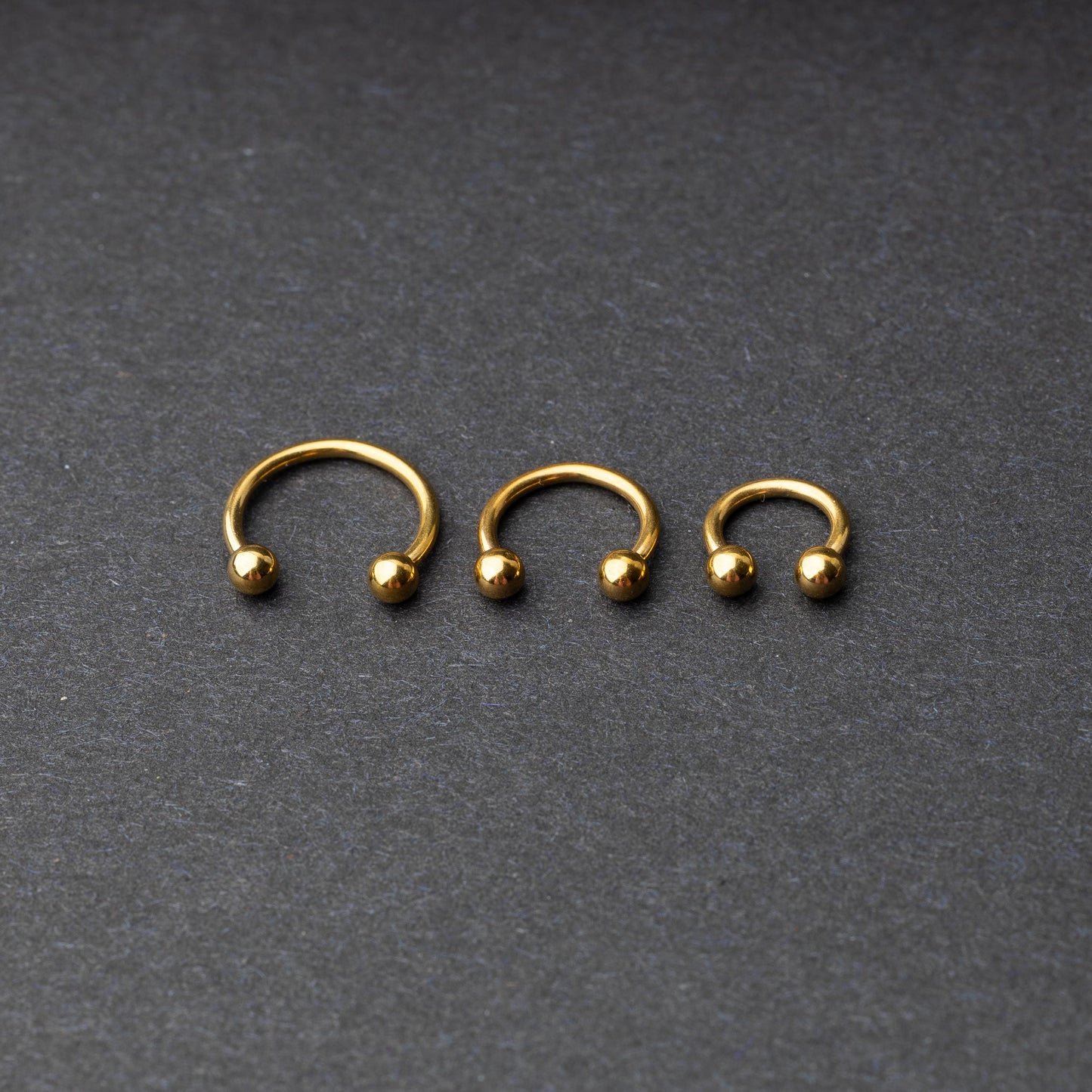 Gold horseshoe rings in three different sizes with ball ends, displayed on a dark background.