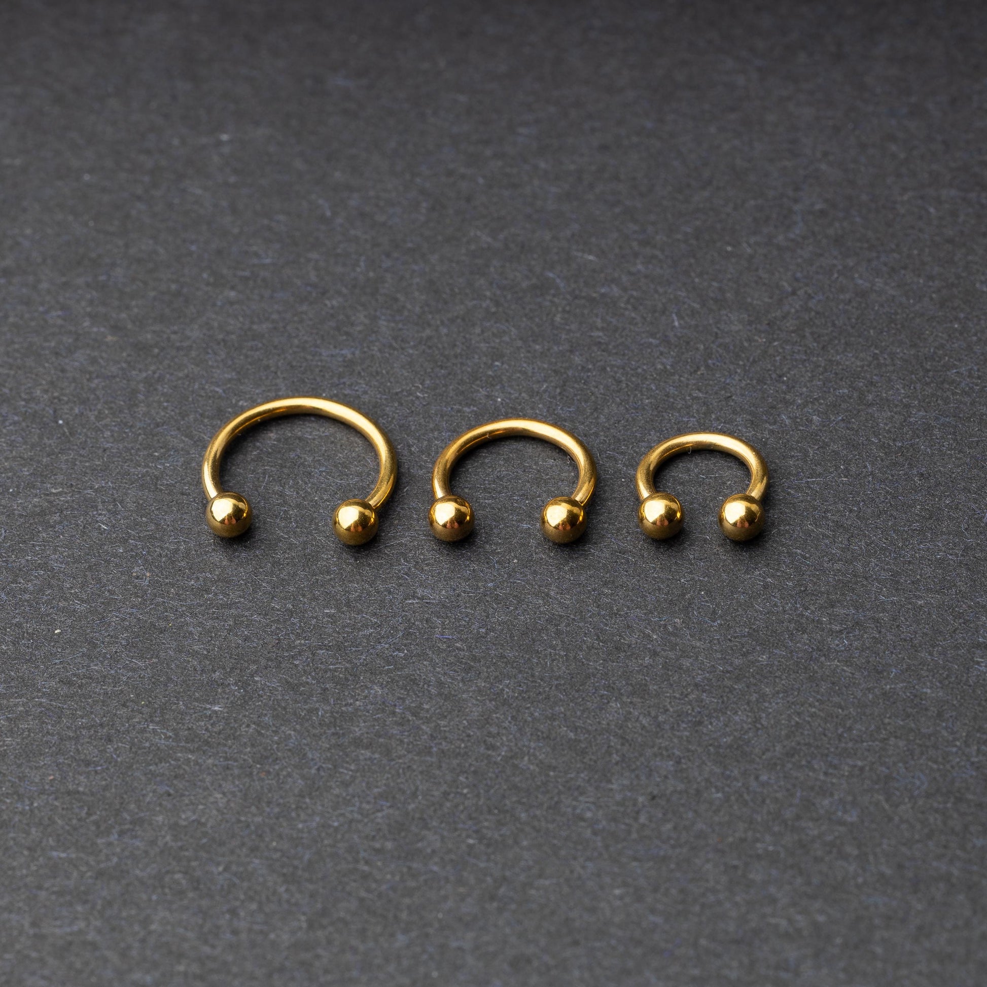 Gold horseshoe rings in three different sizes with ball ends, displayed on a dark background.