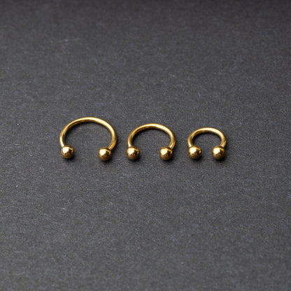 Gold horseshoe rings in three different sizes with ball ends, displayed on a dark background.