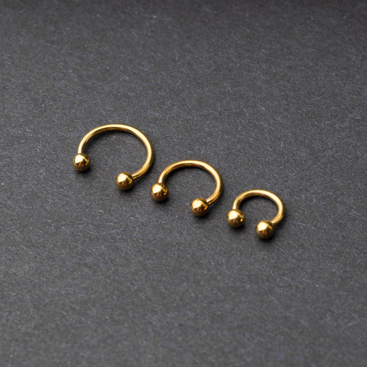 Gold horseshoe rings in three different sizes with ball ends, displayed on a dark background.
