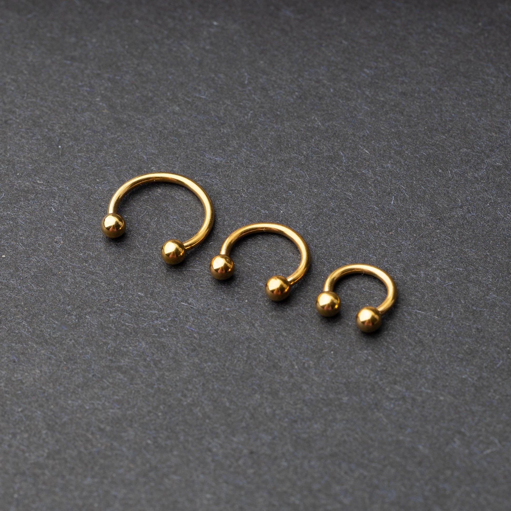 Gold horseshoe rings in three different sizes with ball ends, displayed on a dark background.