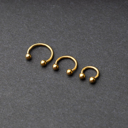 Gold horseshoe rings in three different sizes with ball ends, displayed on a dark background.