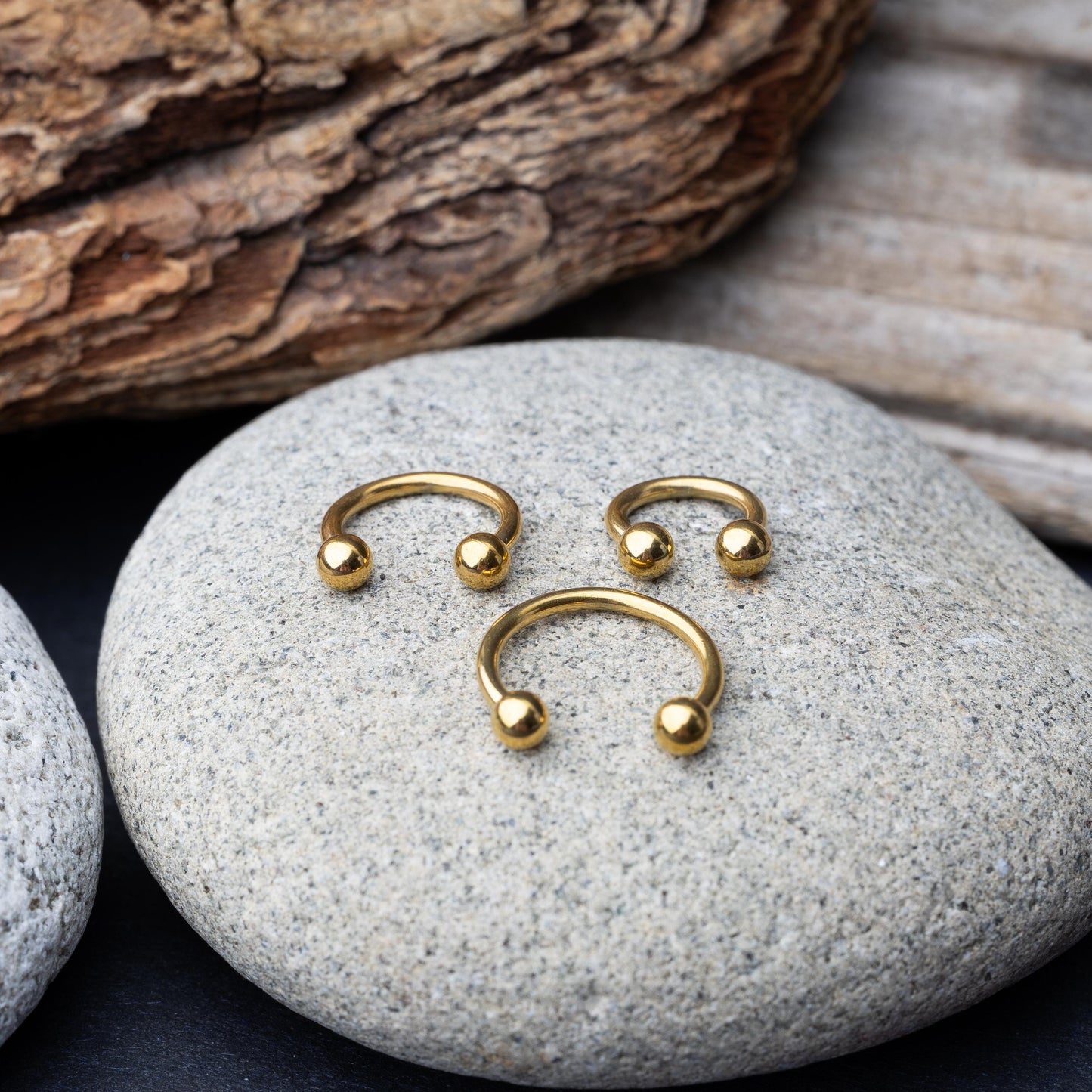 Gold horseshoe rings in three different sizes with ball ends, displayed on a rock.