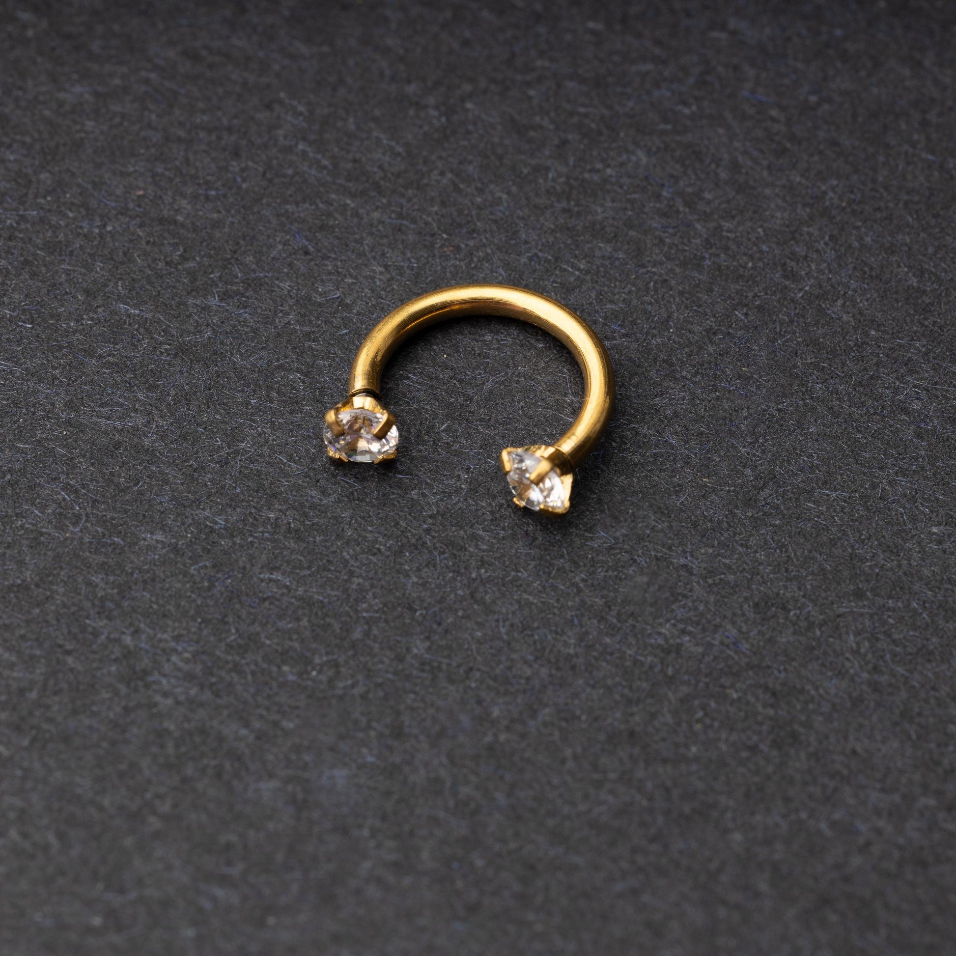 A gold jewelled horseshoe hoop with gemstone ends, displayed on a dark background.