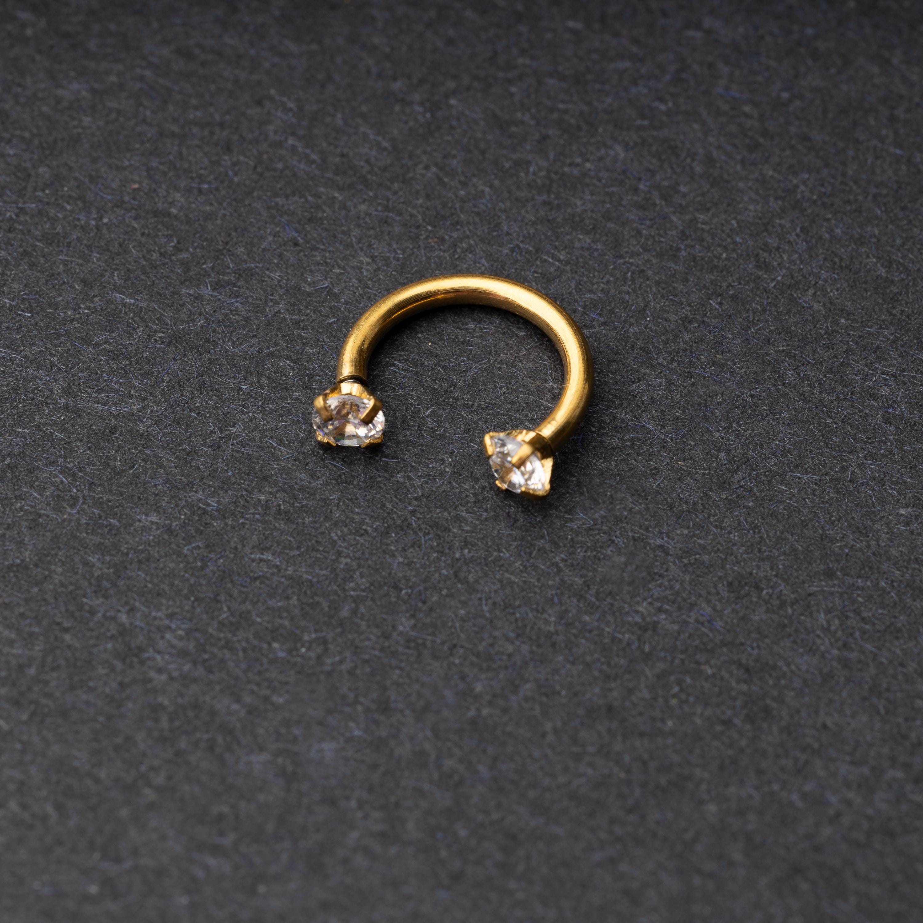 A gold jewelled horseshoe hoop with gemstone ends, displayed on a dark background.