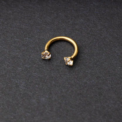 A gold jewelled horseshoe hoop with gemstone ends, displayed on a dark background.