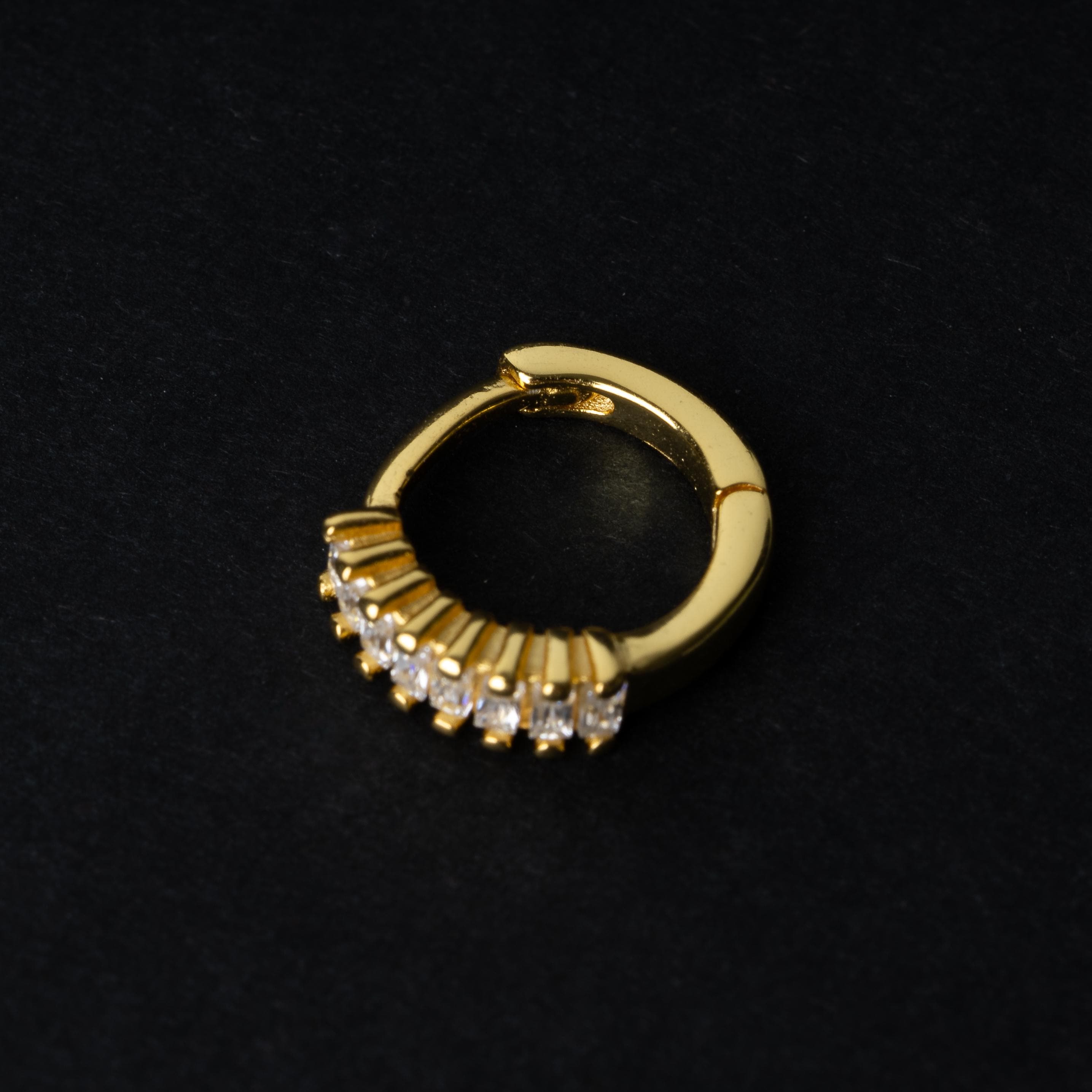 A gold septum clicker featuring a row of sparkling cubic zirconia gemstones, displayed on a black background.