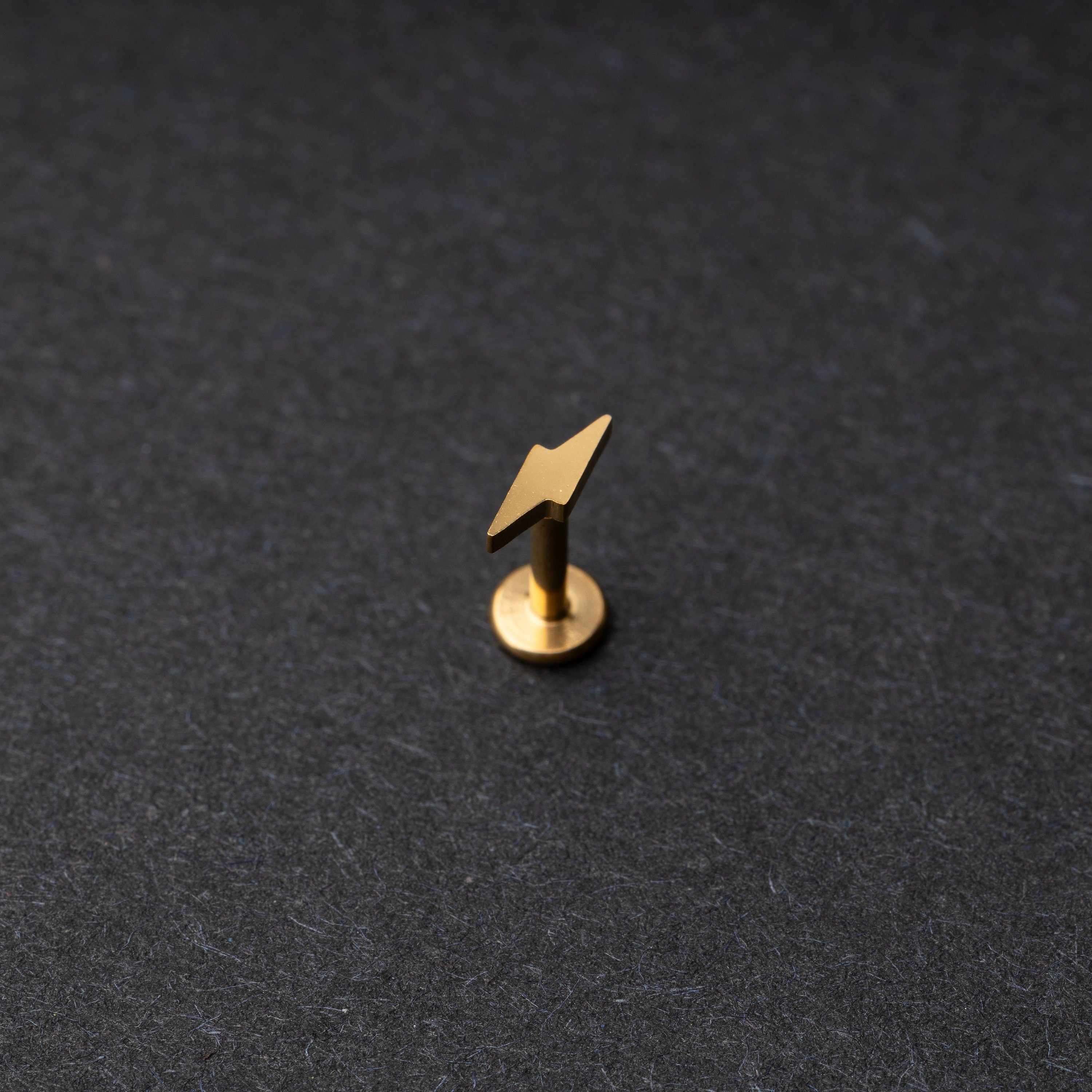 Minimalist lightning bolt labret studs in gold displayed on a dark background.