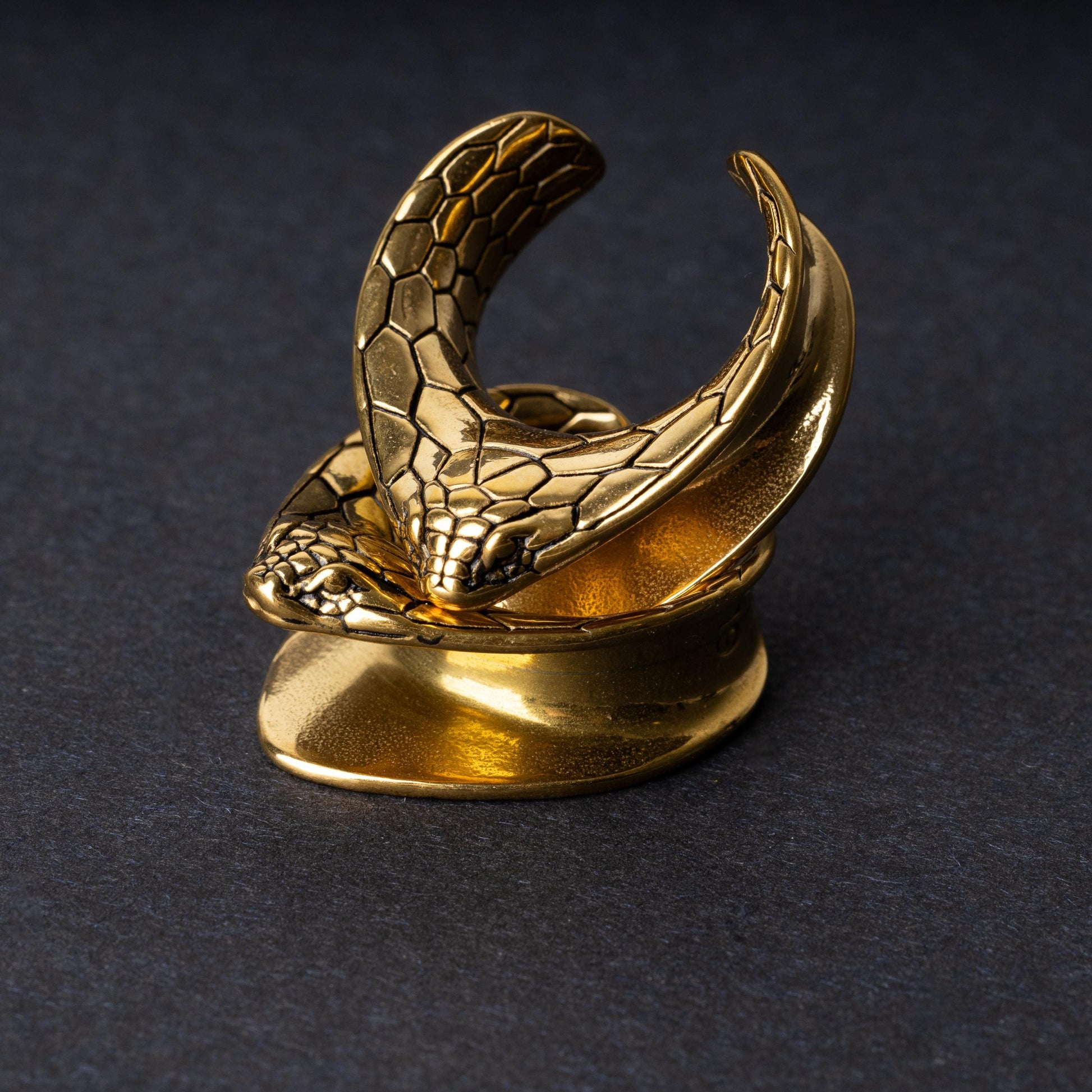 A pair of snakehead saddle tunnels for stretched ears in gold, displayed on a dark background.
