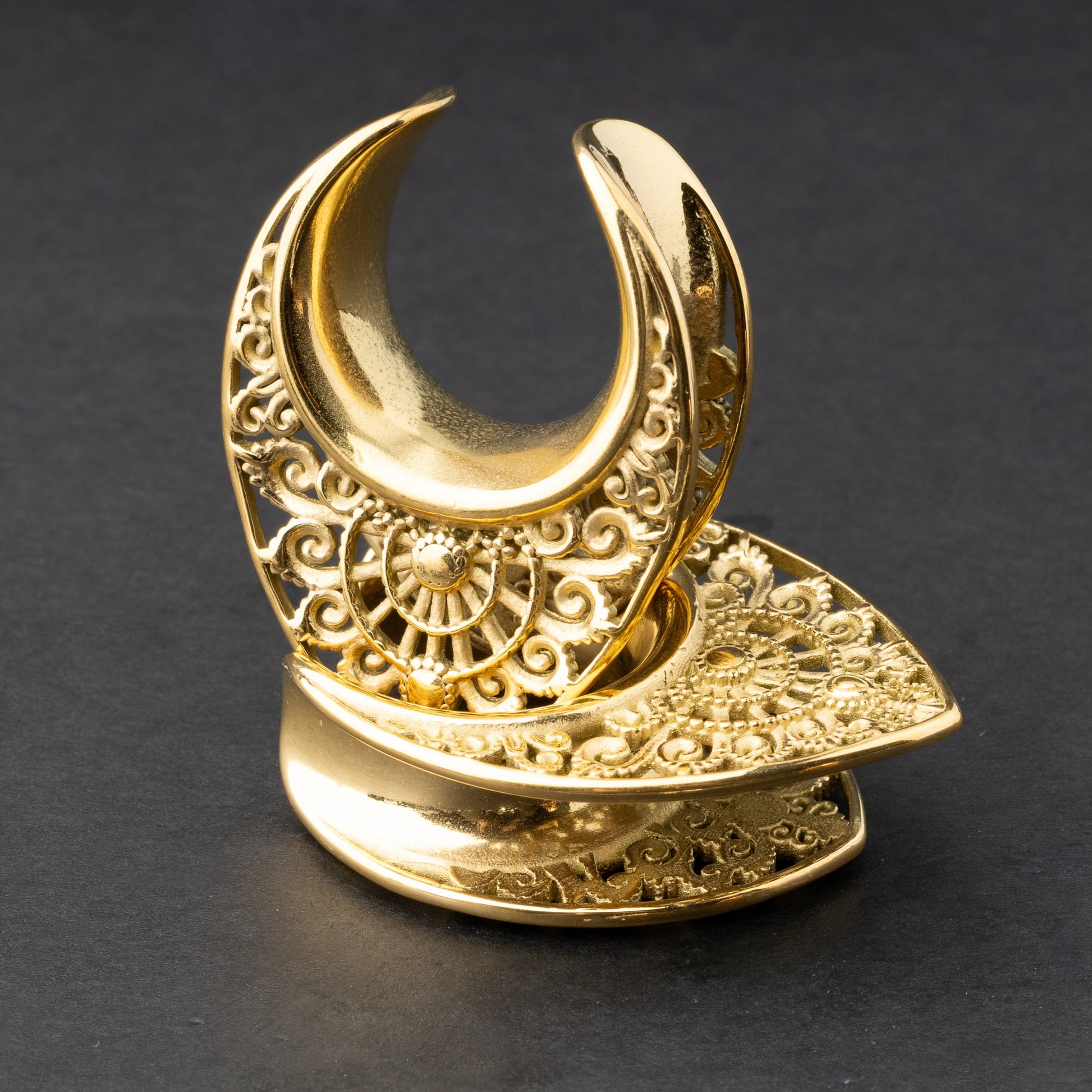 Crescent moon plugs for stretched ears in gold, displayed against a dark background.