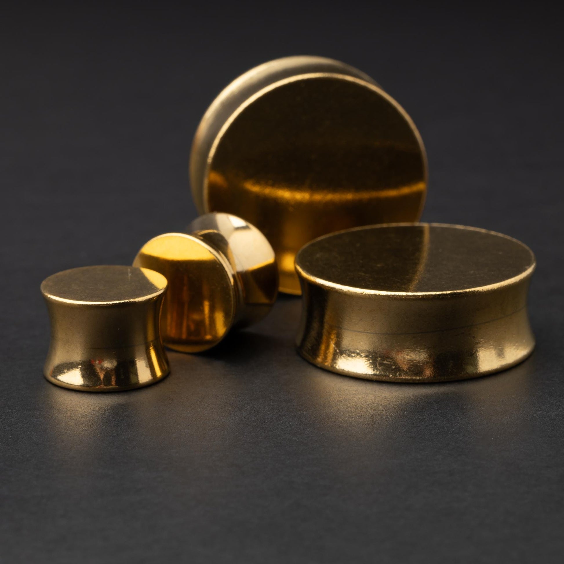 Polished gold plugs in varying sizes, displayed on a dark background.