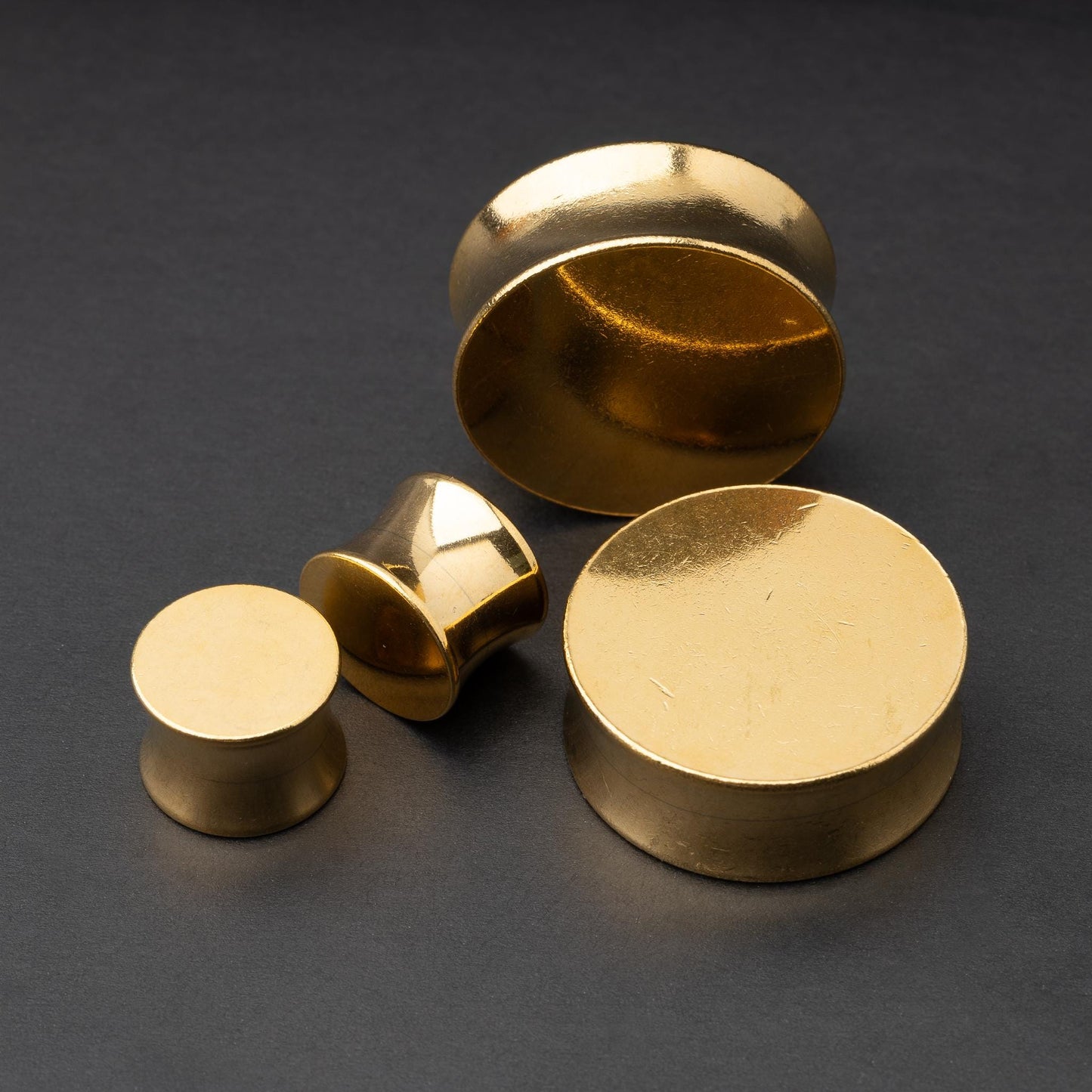 Polished gold plugs in varying sizes, displayed on a dark background.