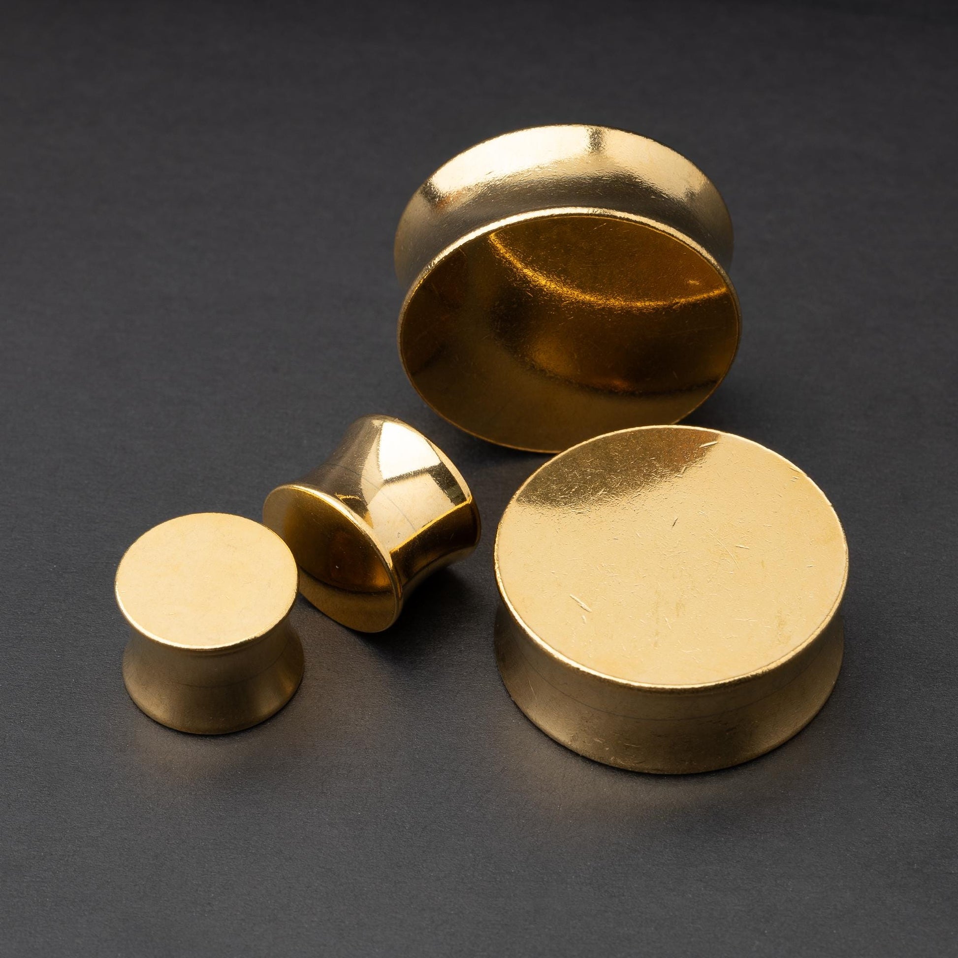 Polished gold plugs in varying sizes, displayed on a dark background.