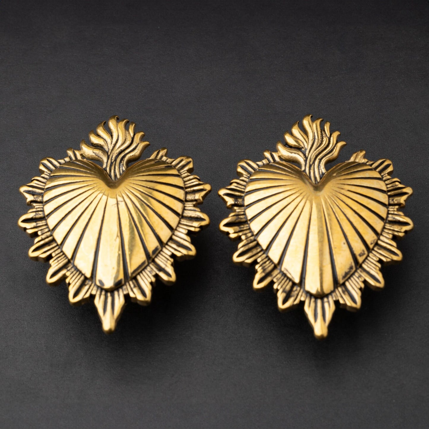 Sacred Heart-inspired plugs in gold, displayed on a matte dark background, showcasing intricate detailing and a bold design.